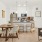 A contemporary kitchen and dining area with light wood floors, white cabinetry, stainless steel appliances, a round dining table with beige chairs, and pendant lights over the island