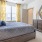 A bedroom with a large bed, gray bedding, blue accent pillows, yellow curtains, a wooden dresser with a decorative mirror, and soft natural light from the windows