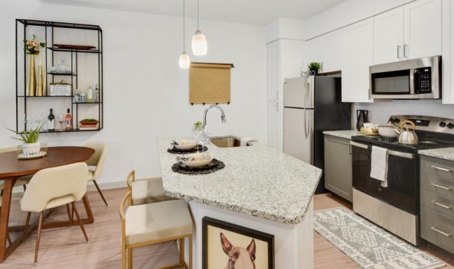 A modern kitchen with white cabinets, stainless steel appliances, a granite countertop island with bar seating, and a small dining area with a round wooden table