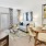 A stylish living and dining area with light wood floors, a beige sofa, abstract wall art, patterned curtains, a round dining table with beige chairs, and wall-mounted shelves